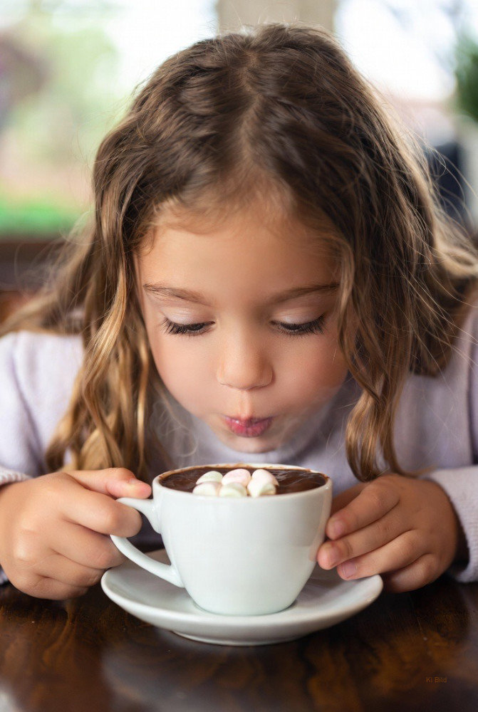 KI Bild - ein junges Mädchen pustet die heiße Milch kälter, nachdem die Schokolade des melting Snowman in der Milch geschmolzen ist und die Marshmallows zum Vorschein gekommen sind.